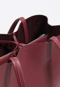 Torebka typu tote w głębokim burgundowym kolorze ze skórzanym wykończeniem o fakturowanej powierzchni. Wnętrze zawiera kieszeń na zamek błyskawiczny oraz podwójne uchwyty dla wygodnego noszenia.