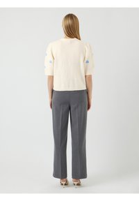 Kort crème gebreid sweater met pofmouwen en blauwe borduursels, gecombineerd met hoge taille grijze broeken en een taps toelopend ontwerp.