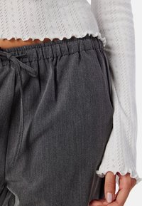 Grijze, geweven stofbroeken met een elastische tailleband en trekkoorddetail, gecombineerd met een witte, geribde top met gaatjespatronen.