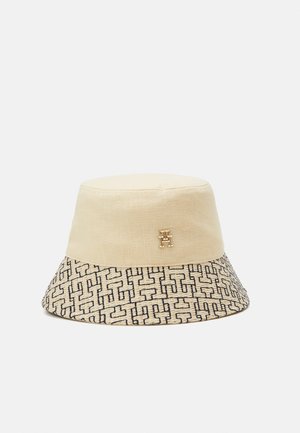 Beige bucket hat with a patterned brim featuring black interlocking T shapes and a small gold double-T logo on the crown.