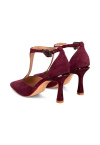 Burgundowe zamszowe buty na wysokim obcasie z ostrym noskiem, paskiem wokół kostki i ozdobnymi elementami. Posiadają smukły obcas typu stiletto oraz otwarty tył.
