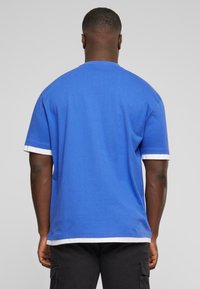 T-shirt bleu à manches courtes en coton, avec des accents blancs sur les manches et l'ourlet. Encolure ronde simple et coupe décontractée.