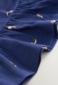 Marineblauer Stoff mit gerafftem Saum und kleinen, bunten Segelbootmustern. Weiche Textur mit sauberen Nähdetails.