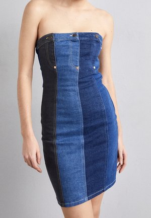 Mini sukienka bez ramiączek, dopasowana, z pionowymi panelami z denimu w różnych odcieniach niebieskiego i czarnego, na stojącej osobie na jednolitym tle.