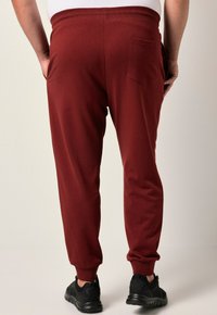 Bordeauxkleurige sportbroek met een elastische tailleband, taps toelopende pijpen en een achterzak. Draag het met zwarte sportschoenen.