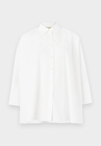 Balta pogca krekls ar klasisku apkakli, garām piedurknēm un brīvu piegriezumu. Gluda kokvilnas auduma, bez redzamām rakstu vai akcentu detaļām.