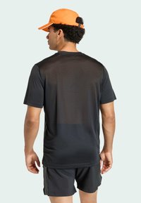 Zwart sportshirt met een mesh rug, gecombineerd met zwarte shorts. Een fel oranje pet maakt de outfit compleet, voorzien van een verstelbare band aan de achterkant.