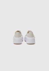 Lyse beige lerretsko med teksturert overflate, hvite tykke gummisåler og detaljering på hælen. Minimalistisk design uten synlige aksenter.