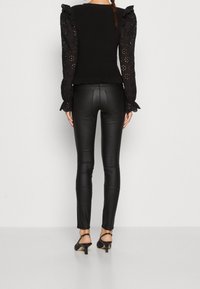 Svart topp med puffärmar i ögla-mönster, texturerad bodice med volangslut; ihop med figurnära svarta läderbyxor och svarta klackskor.