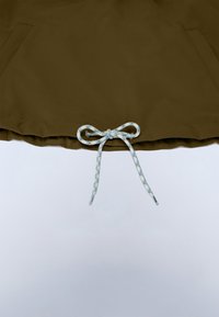 Brunt tøjstykke med forlommer foran og en blå-hvid snor bundet i en sløjfe ved kanten mod en hvid baggrund.