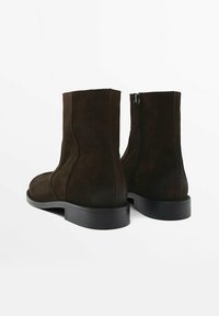 Bottines en daim marron foncé à texture lisse, bout arrondi, et semelle extérieure en caoutchouc noir solide. Design minimaliste sans éléments métalliques visibles.