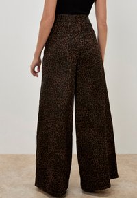 Weite Hosen in Dunkelbraun mit schwarzem Leopardenmuster. Merkmale sind ein hoher Bund, zwei Gesäßtaschen und eine glatte Textur.