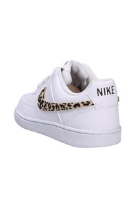 White Nike shoes with a textured leather upper, featuring a leopard print swoosh and a flat rubber sole. Accents include a branded heel tag.
