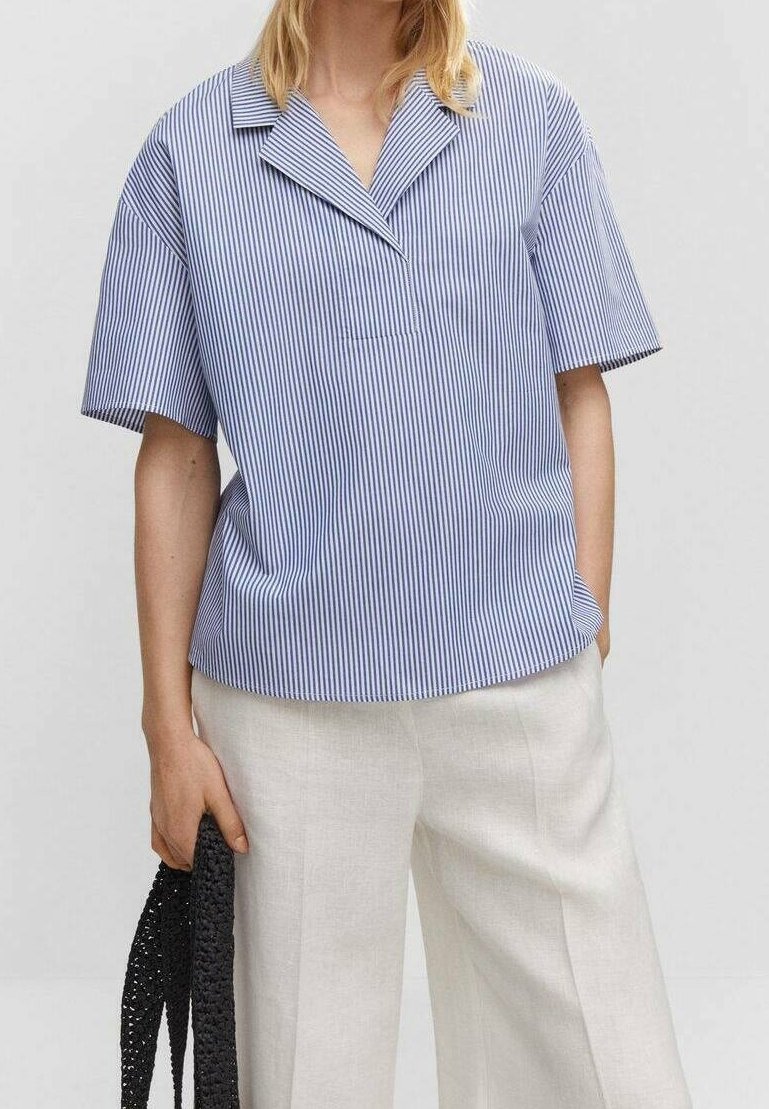 Personne portant une chemise à manches courtes rayée verticale bleu et blanc et un pantalon beige clair, tenant un sac tissé noir dans une main.