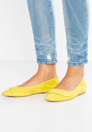 Gule ruskindspidse flade sko båret med lyseblå revnede skinny jeans vist fra siden.