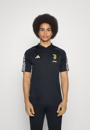 Schwarzes Sporttrikot mit gelben Akzenten, hoher Kragen, kurzen Ärmeln und drei weißen Streifen an jedem Ärmel. Logo-Details enthalten.