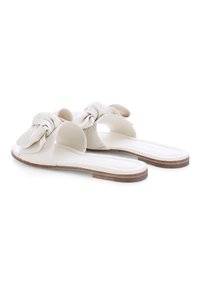 White flat slide sandals with knotted leather straps and wooden low heels, shown from a three-quarter rear angle on a white background.