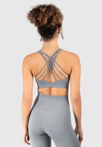 Szary stanik sportowy z krzyżującymi się ramiączkami z tyłu, wykonany z gładkiej elastycznej tkaniny, w połączeniu z pasującymi legginsami o wysokim staniek.
