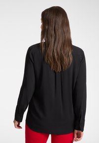 Czarna bluzka z długim rękawem z mankietami na guziki, miękka tkanina, tylny zakładka, noszona z czerwonymi spodniami, prezentująca gładką fakturę i luźny krój.