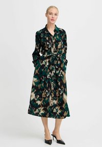 Abito lungo con bottoni in verde, nero e beige a stampa animale, con vita cinturata, maniche lunghe e tasche laterali. Texture setosa.