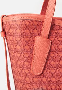 Coral leather tote bag featuring an embossed pattern, smooth texture, and a sturdy strap with contrasting stitching detail.