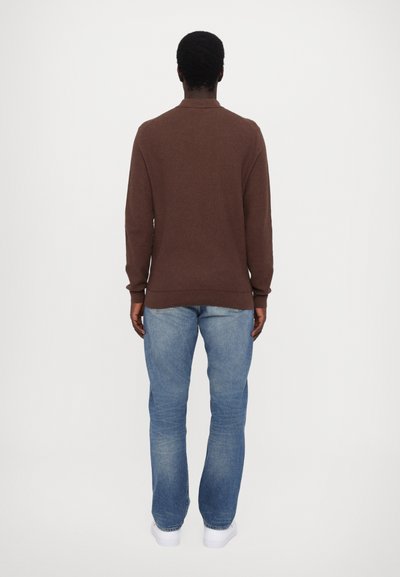 Brun sweater med høj krave, parret med lyseblå jeans. Optrædendet har et enkelt, struktureret design og en afslappet pasform.