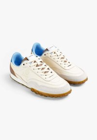 Baskets en cuir beige avec des accents bleus, semelle texturée, design à lacets et branding subtil sur le côté. Dotées d'un col rembourré.