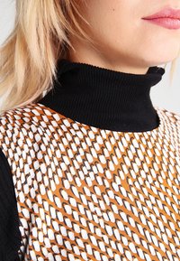 Monivärinen kuvioitu mekko, jossa on ruskea, valkoinen ja musta abstrakti kuvio, mustalla ribatulla korkealla kauluksella.