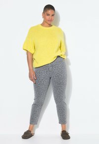 Suéter de punto amarillo con mangas cortas, combinado con pantalones grises de estampado de leopardo y zapatos tipo slip-on marrones. Textura suave y ajuste relajado.