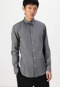 Camisa de botones gris hecha de una tela suave, con cuello y siete botones en la parte delantera. Mangas largas con puños abotonados.