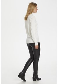 Bijela rolka uparena s crnim skinny farmerkama od umjetne kože i čizmama do gležnja. Pulover ima rebraste rubove; elegantan je i prilagođen.