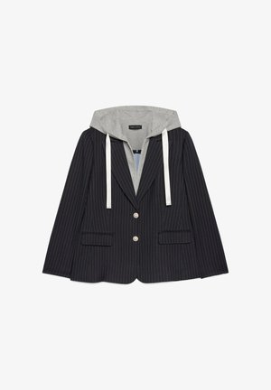 Blazer nero a righe con due bottoni frontali e tasche a pattina, indossato su una felpa grigia con cappuccio e stringhe bianche.