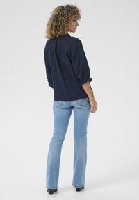 Navy blue blouse with a gathered neckline, three-quarter sleeves, and textured fabric paired with light blue flared jeans. Black footwear.