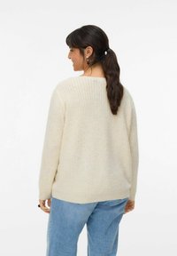 Light beige knitted sweater with a loose fit, featuring a wide neckline and subtle texture. Worn with light blue denim jeans.