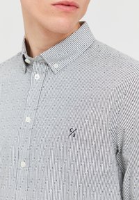 Camicia a manica lunga con motivo a righe in bianco e nero, dotata di un piccolo logo sulla tasca del petto e colletto a punta.