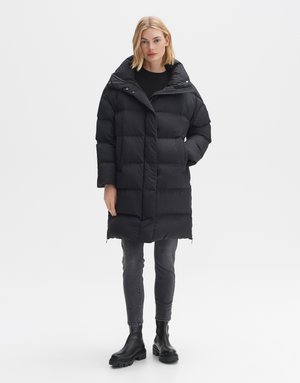 Schwarze gepolsterte Jacke mit hohem Kragen, ausgestattet mit horizontalen Nähten und Reißverschlusstaschen. Über einem schwarzen Pullover und grauen Slim-Jeans getragen, kombiniert mit schwarzen Stiefeln.