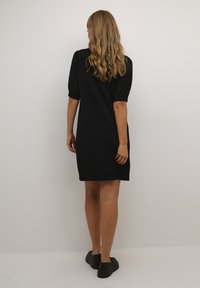 Abito nero a maniche corte con una vestibilità rilassata e scollatura rotonda. Tessuto liscio di un solo colore, che arriva a metà coscia. Indossato con scarpe nere.