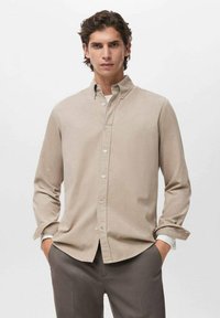 Camisa abotonada beige de mangas largas, hecha de una tela suave. Presenta un cuello clásico y un ajuste holgado. Diseño liso, con un detalle mínimo.