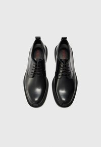 Black leather shoes with a smooth finish, rounded toe, lace-up design, and contrasting black rubber sole. Interior features red logo text.