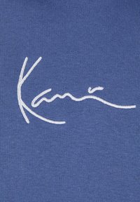 Il tessuto blu presenta un testo firmato ricamato bianco, mostrando una consistenza liscia e un design di peso medio. Non sono presenti altri motivi o accenti.