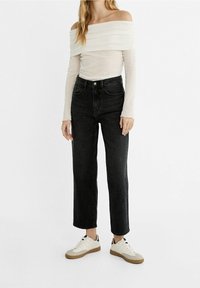 Top blanco sin mangas, con largos en los hombros, combinado con unos vaqueros negros de pierna recta y cintura alta, y zapatillas blancas con suela beige.