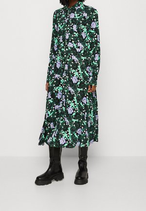 Kobieta ubrana w długą czarną sukienkę w zielone, białe i fioletowe kwiatowe wzory, do której dobrała czarne masywne kozaki do kolan.