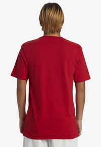 Camiseta roja de manga corta hecha de algodón, con cuello redondo y corte recto. Sin logotipos ni patrones visibles; textura suave.