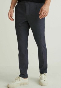 Ciemnogranatowe spodnie wykonane z teksturowanej tkaniny, z prostym przodem, prostą nogawką i bocznymi kieszeniami, zestawione z białymi trampkami.