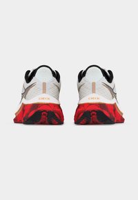 Ζευγάρι λευκά αθλητικά παπούτσια με μαύρο επένδυση, χρυσές λεπτομέρειες και κόκκινες σόλες με σχέδιο, σε θέα από πίσω πάνω σε απλό φόντο.