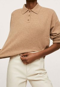 Sweter polo w kolorze camel z dzianiny, z kołnierzykiem i trzema guzikami, w połączeniu z kremowymi spodniami. Miękka faktura i luźny krój.