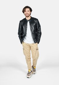 Svart läderjacka, vit t-shirt, beige cargobyxor och flerfärgade sneakers. Jackan har en ficka med dragkedja och rund halsringning.