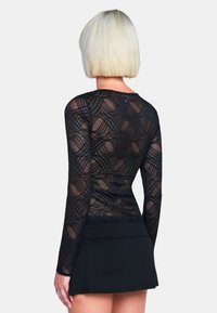 Zwarte lange mouwen top van doorschijnende kant, met een ingewikkeld geometrisch patroon en een aansluitend ontwerp, gecombineerd met een zwarte rok.