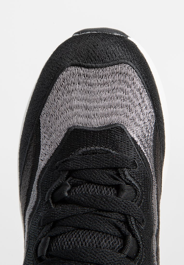 Baskets de sport noires et grises avec un dessus texturé, fermeture à lacets et une semelle intermédiaire blanche. Présente un design lisse et courbé.