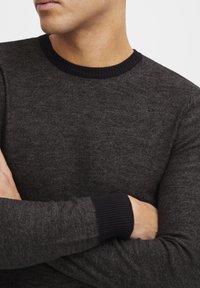 Mørk grå genser med teksturert stoff, med en ribbet svart halskant og mansjetter. Enkelt design med lange ermer og tettsittende fasong.
